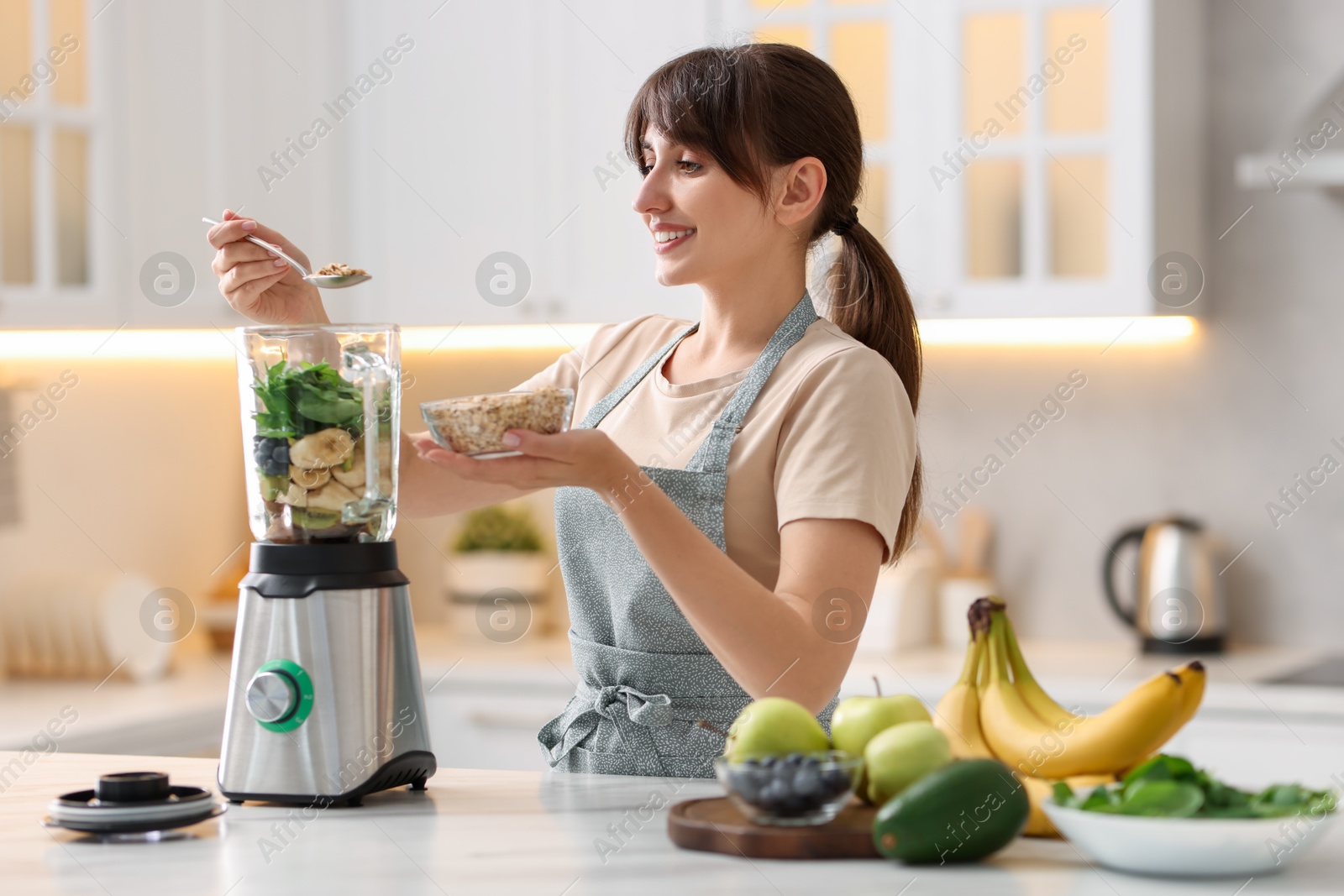 Photo of Young woman making delicious smoothie with blender at white marble table in kitchen