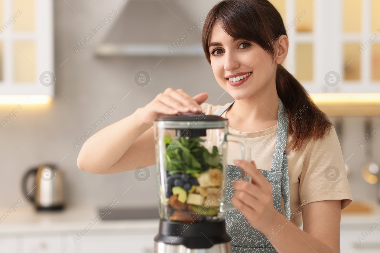 Photo of Young woman making delicious smoothie with blender in kitchen