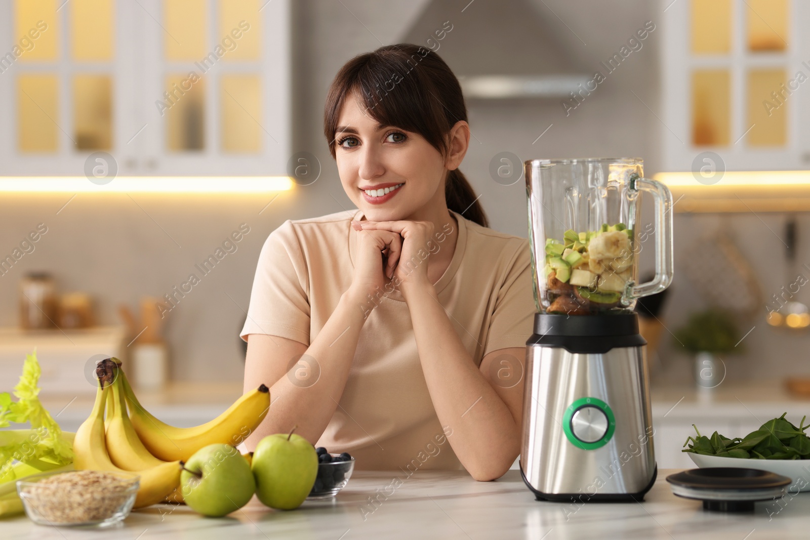 Photo of Young woman making delicious smoothie with blender at white marble table in kitchen