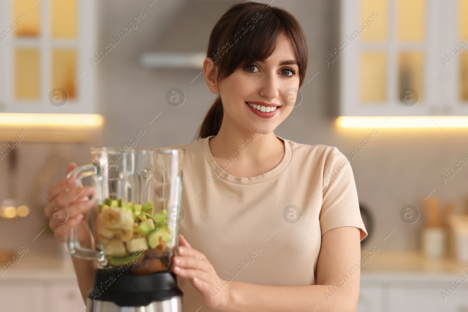 Photo of Young woman making delicious smoothie with blender in kitchen