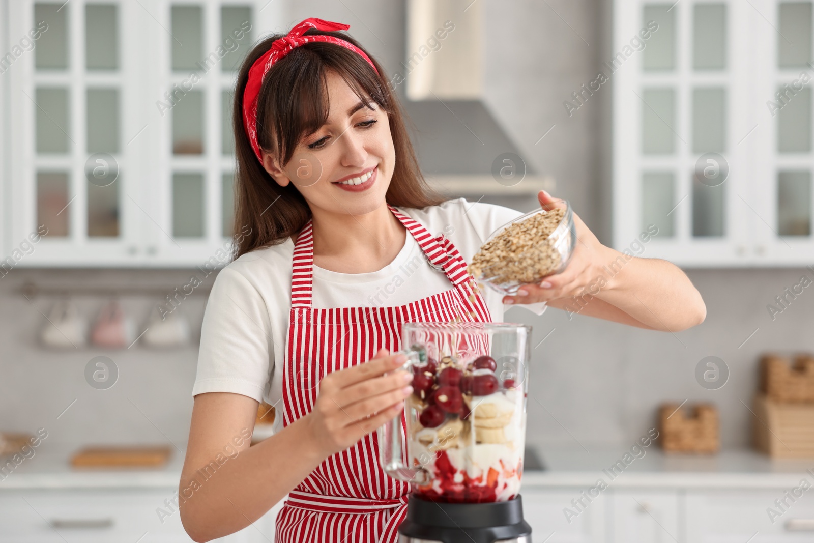 Photo of Young woman making delicious smoothie with blender in kitchen