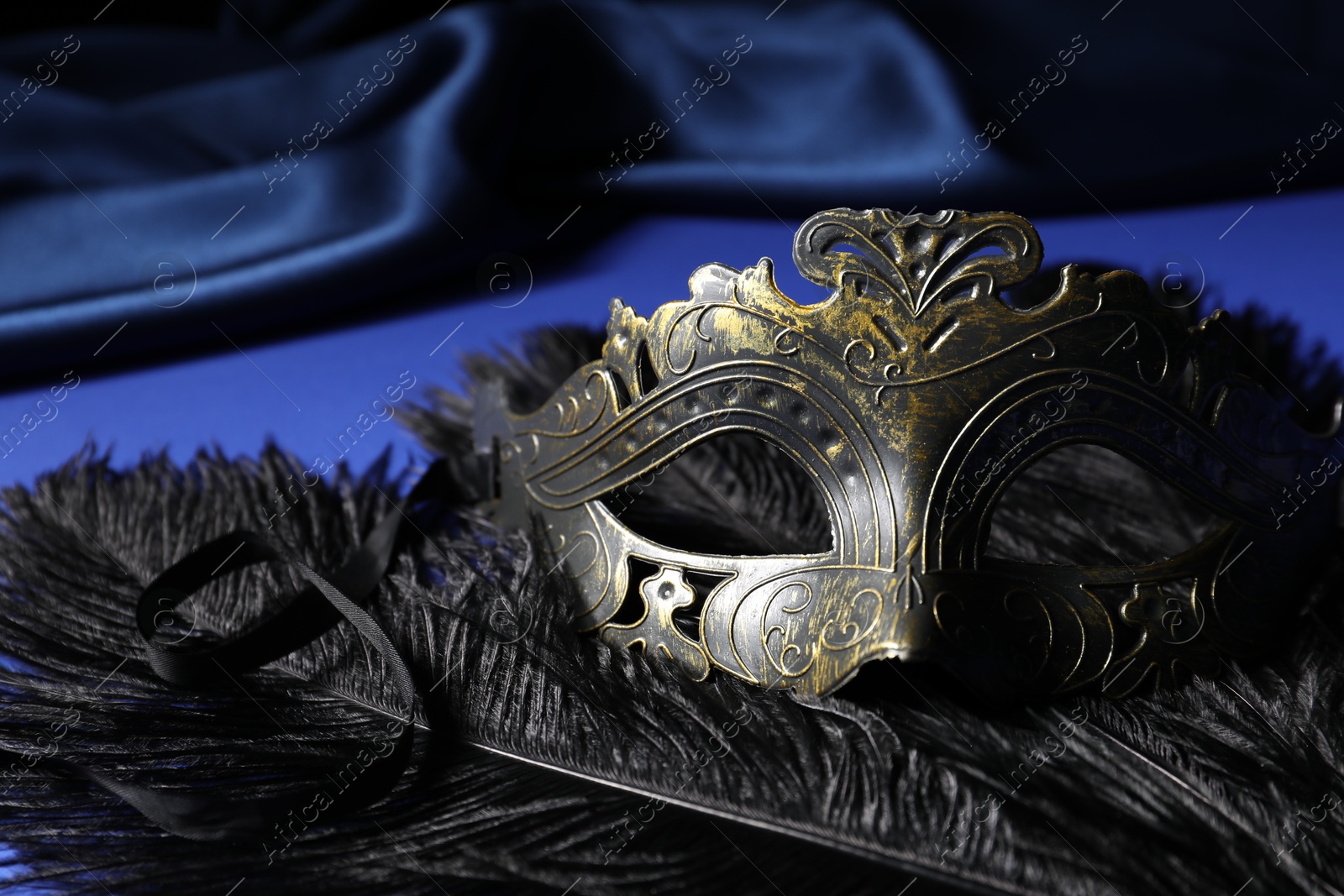 Photo of Beautiful carnival mask and feathers on blue fabric, closeup