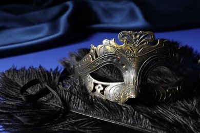 Photo of Beautiful carnival mask and feathers on blue fabric, closeup