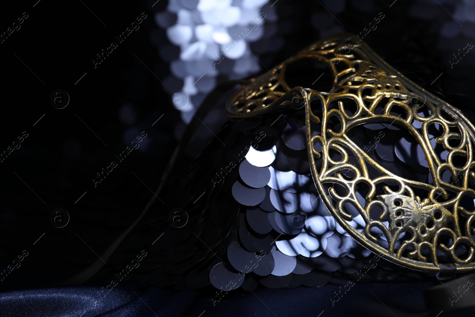 Photo of Beautiful carnival mask and fabric with golden sequins in darkness, closeup