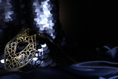 Beautiful carnival mask and fabric with golden sequins in darkness, closeup. Space for text