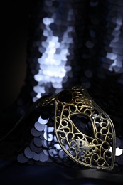 Photo of Beautiful carnival mask and fabric with golden sequins in darkness, closeup