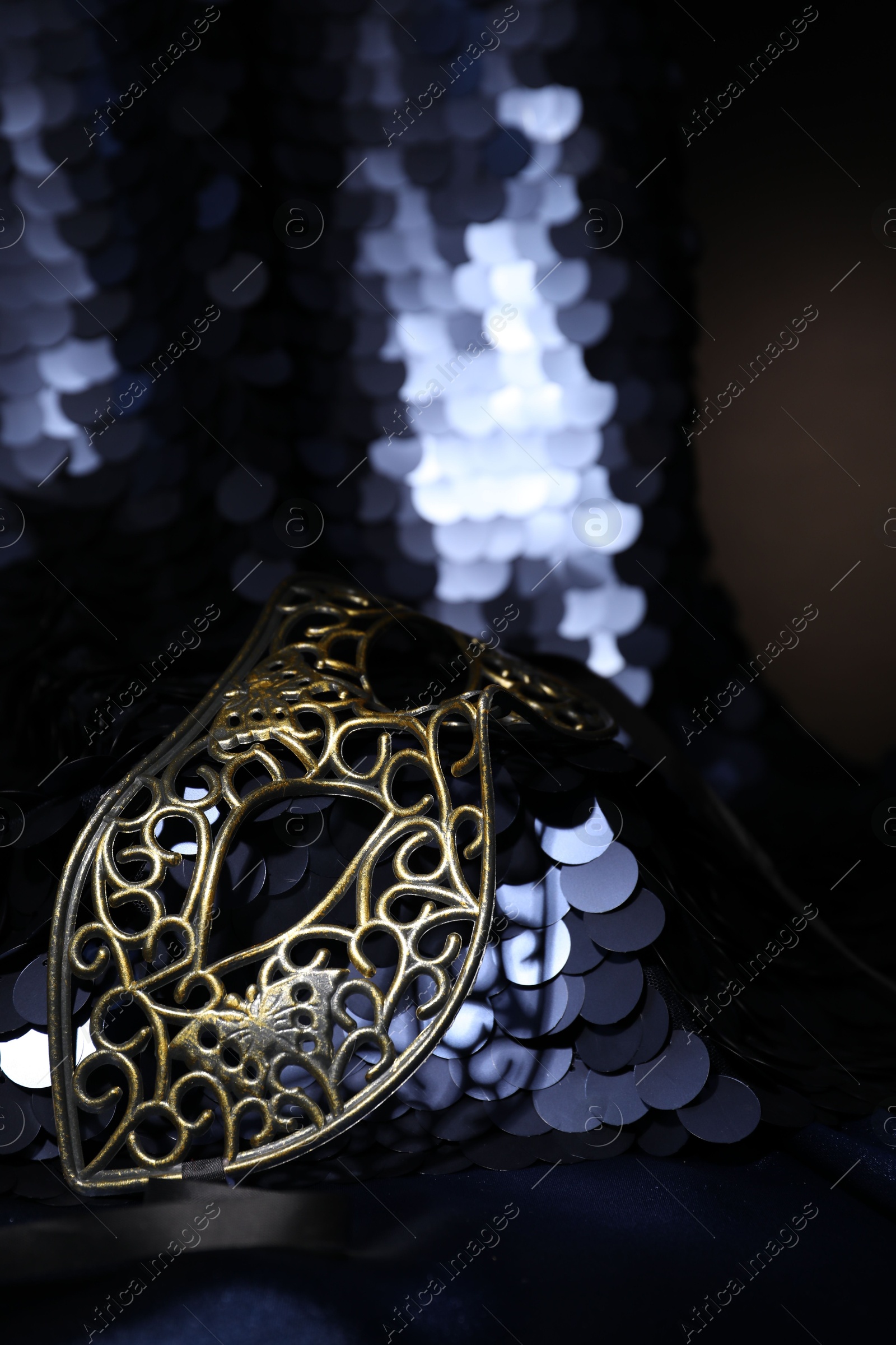 Photo of Beautiful carnival mask and fabric with golden sequins in darkness, closeup