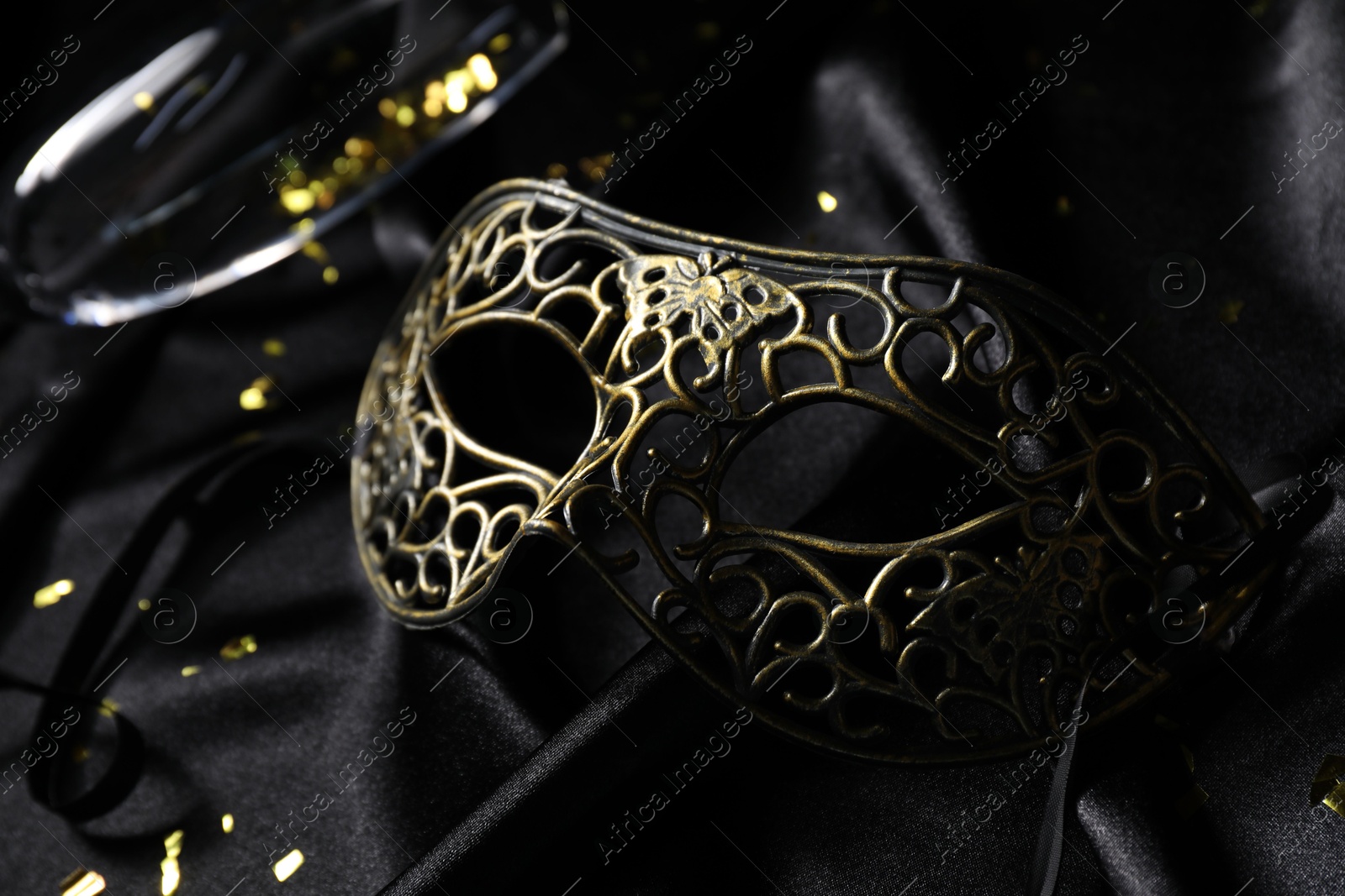 Photo of Beautiful carnival mask on black silk fabric, closeup