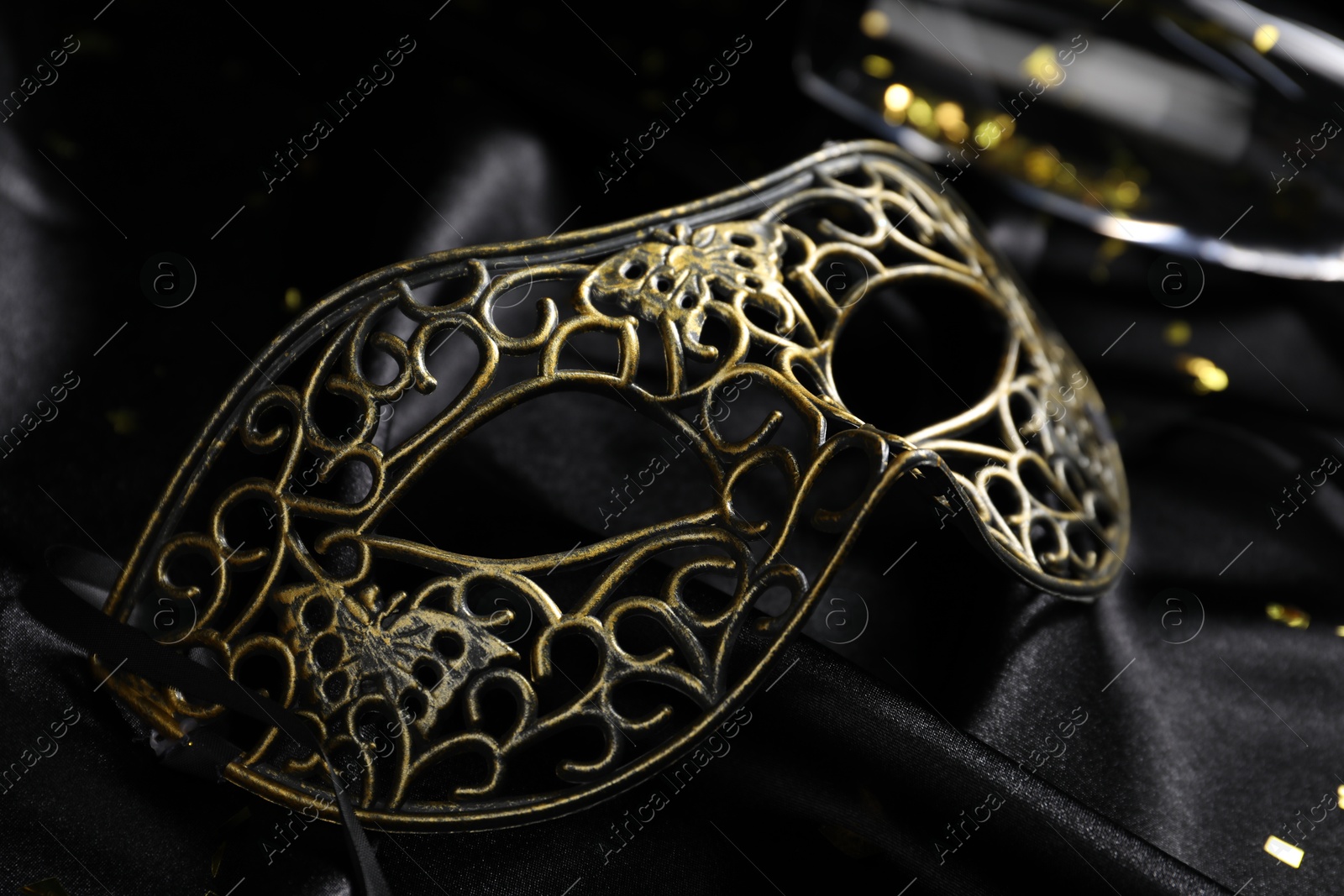 Photo of Beautiful carnival mask on black silk fabric, closeup