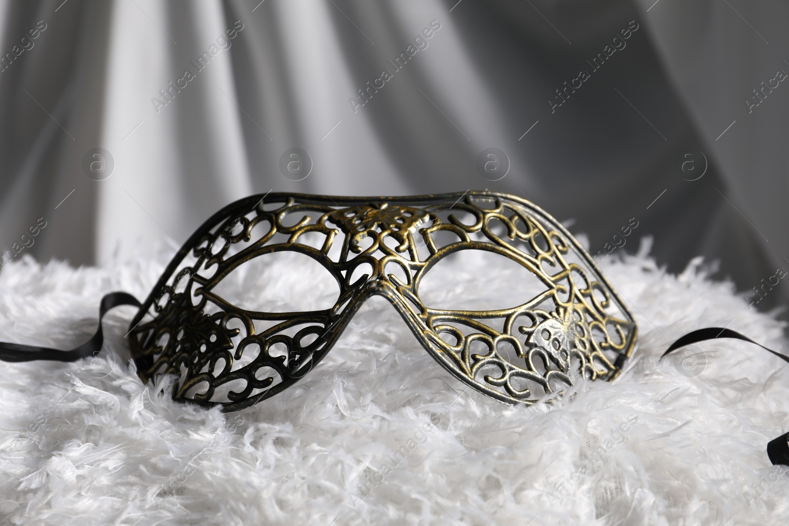 Photo of Beautiful carnival mask on white fabric, closeup