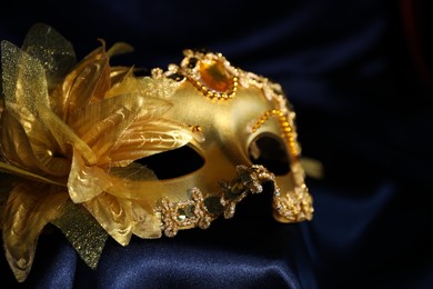 Photo of Beautiful golden carnival mask on blue silk fabric, closeup