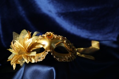 Photo of Beautiful golden carnival mask on blue silk fabric, closeup