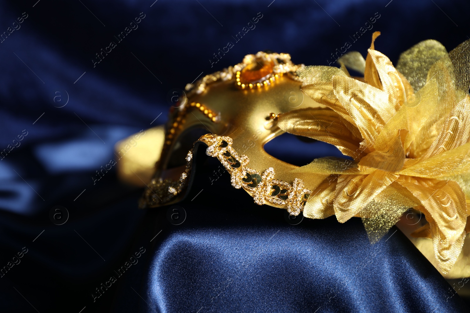 Photo of Beautiful golden carnival mask on blue silk fabric, closeup