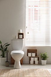 Photo of White toilet bowl, paper rolls and houseplants in bathroom