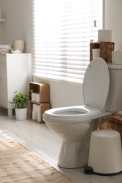 Photo of White toilet bowl, trash can and paper rolls in bathroom