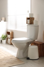 Photo of White toilet bowl, trash can and paper rolls in bathroom