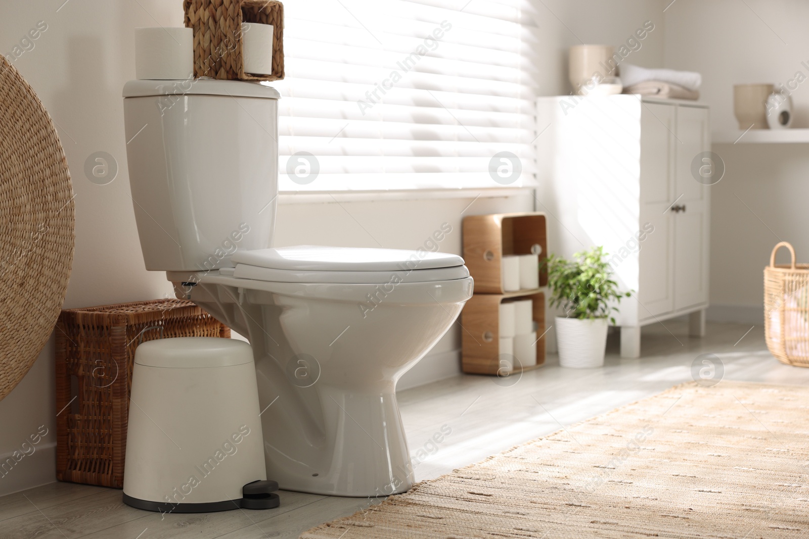 Photo of White toilet bowl, trash can and paper rolls in bathroom