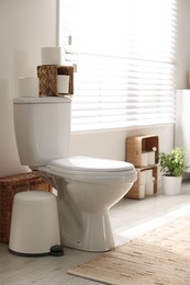 Photo of White toilet bowl, trash can and paper rolls in bathroom