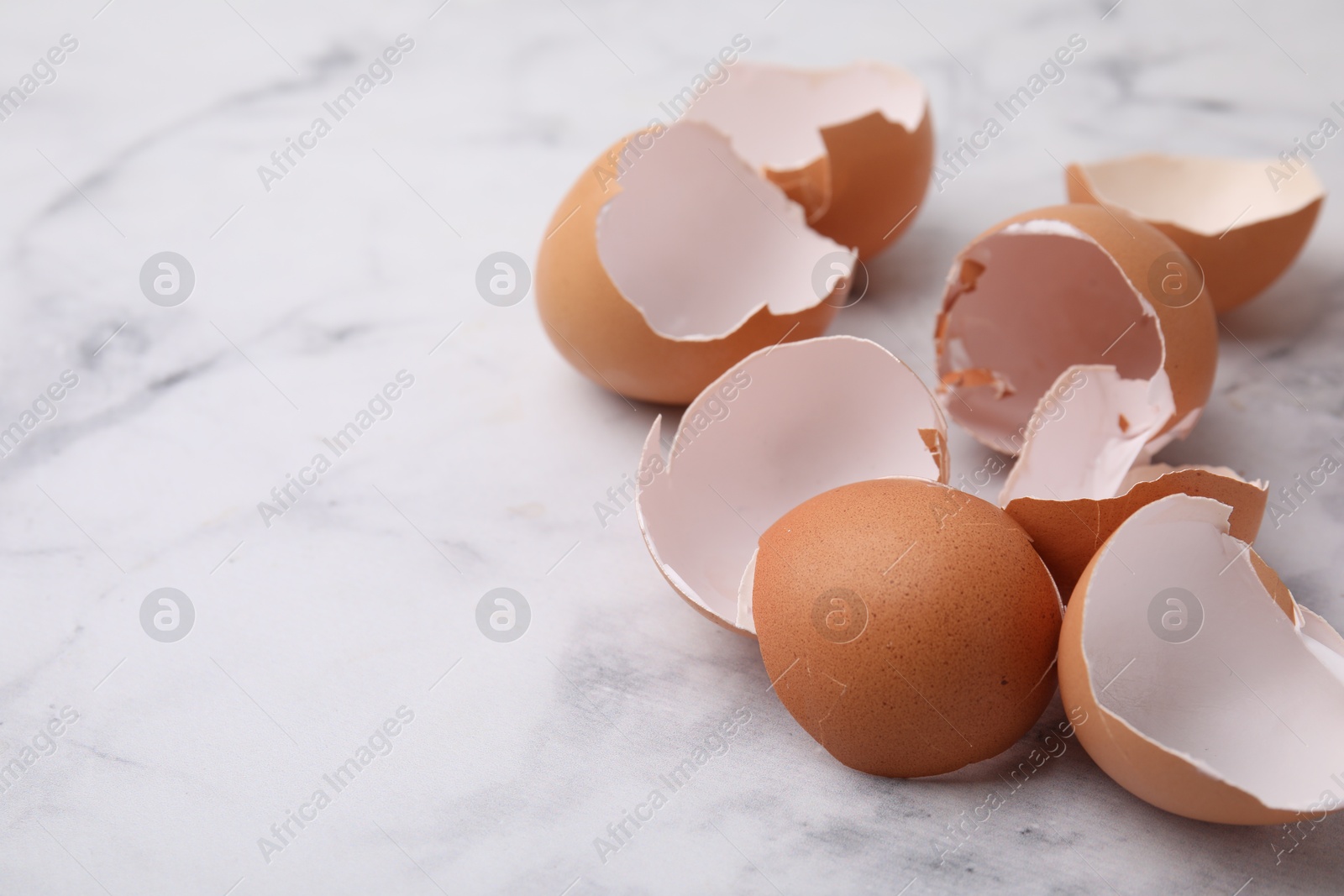 Photo of Broken eggshells on light marble table, closeup. Space for text