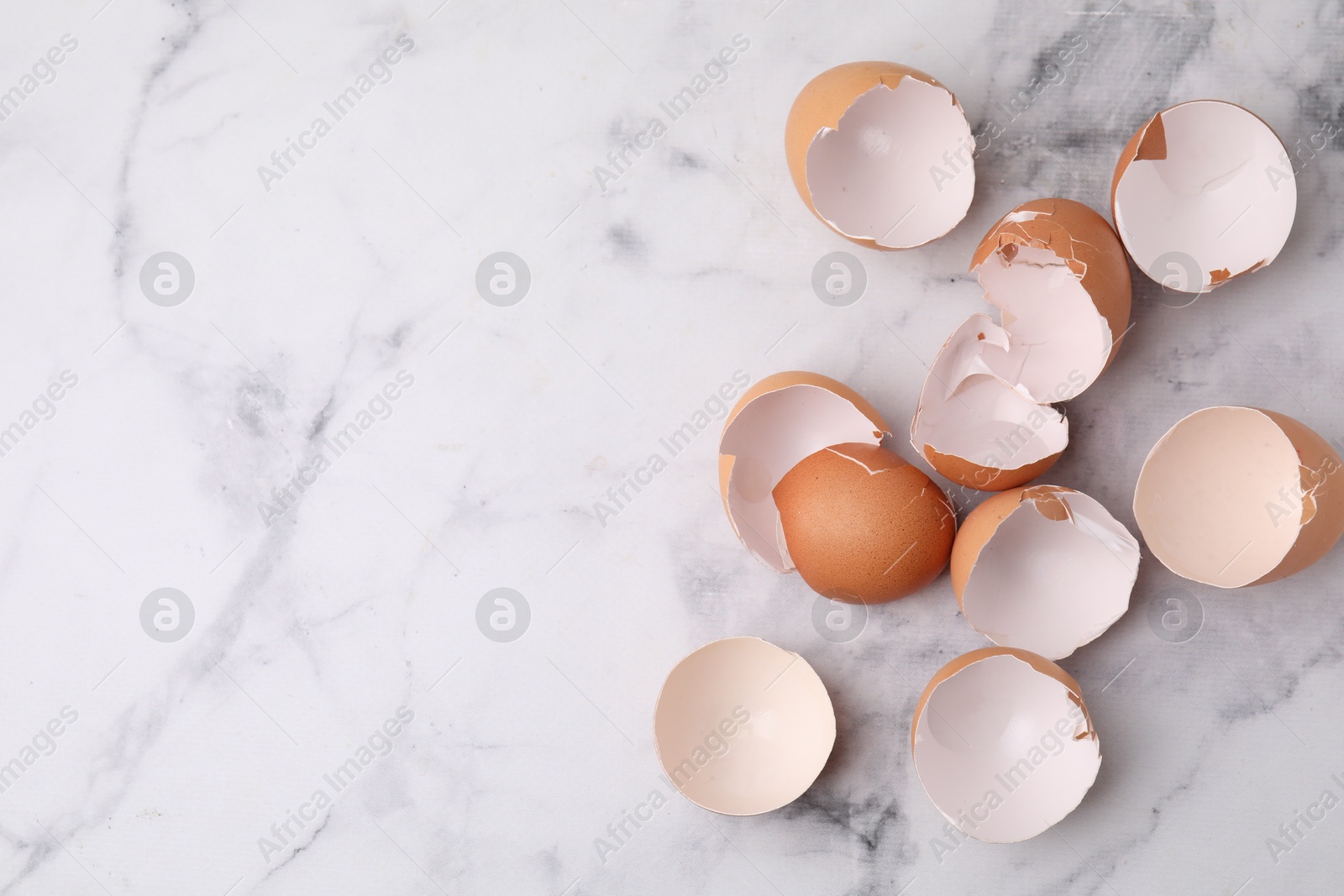 Photo of Broken eggshells on light marble table, top view. Space for text