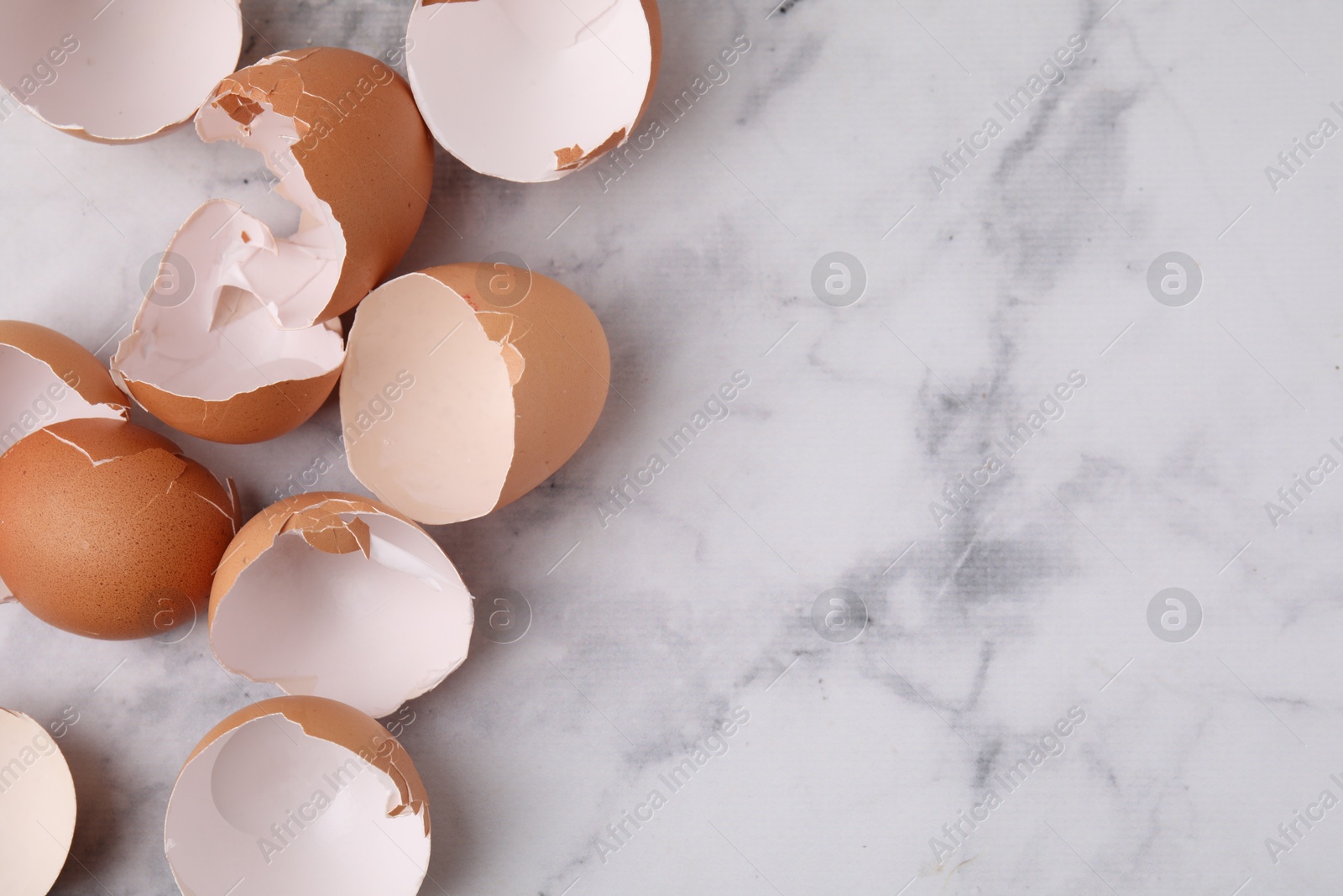 Photo of Broken eggshells on light marble table, top view. Space for text