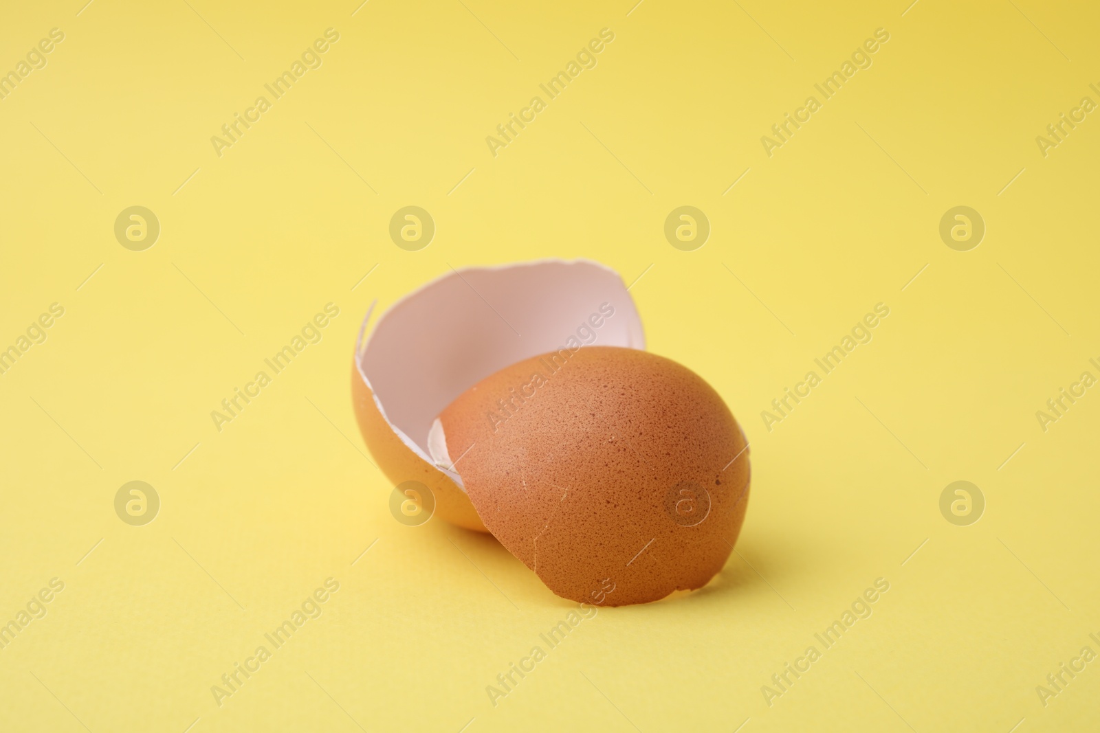 Photo of Pieces of broken eggshells on yellow background, closeup