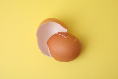 Photo of Pieces of broken eggshells on yellow background, top view