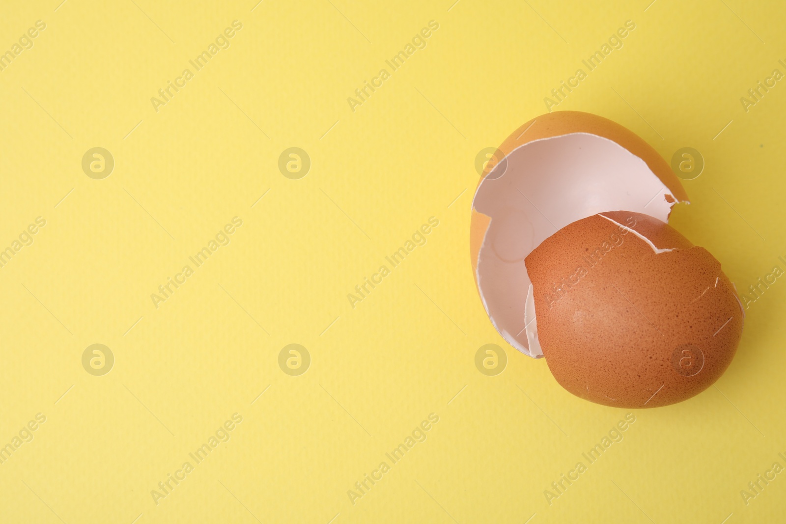 Photo of Pieces of broken eggshells on yellow background, top view. Space for text