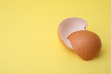 Photo of Pieces of broken eggshells on yellow background, closeup. Space for text