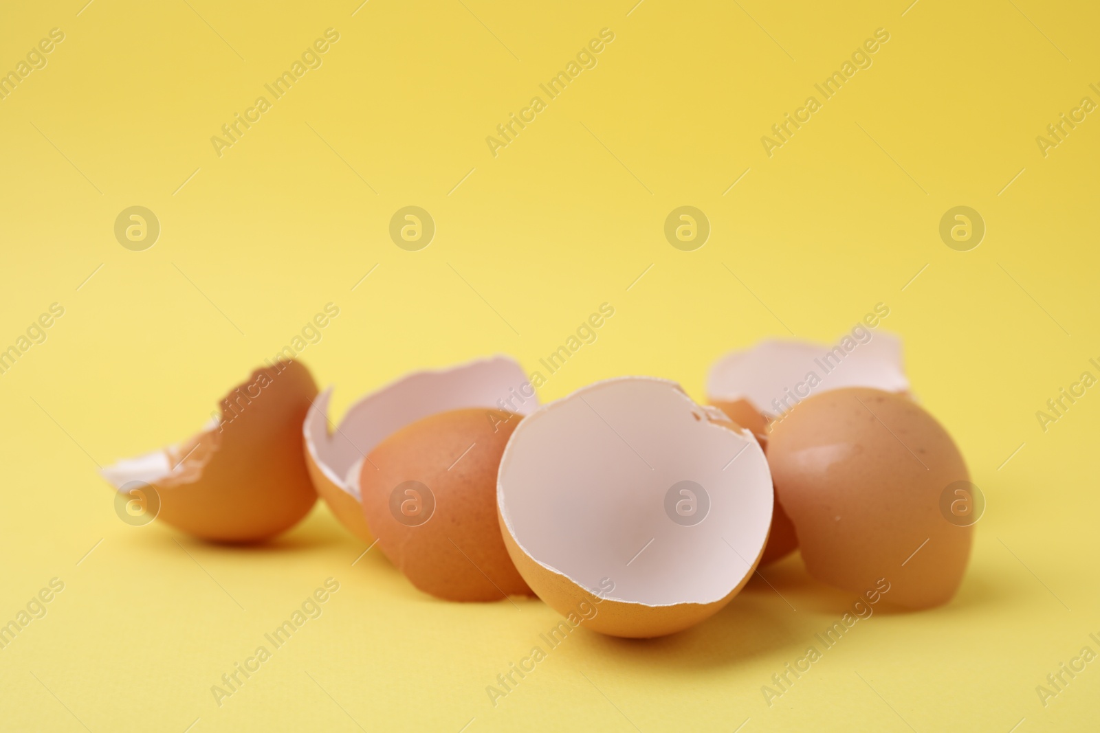 Photo of Pile of broken eggshells on yellow background, closeup