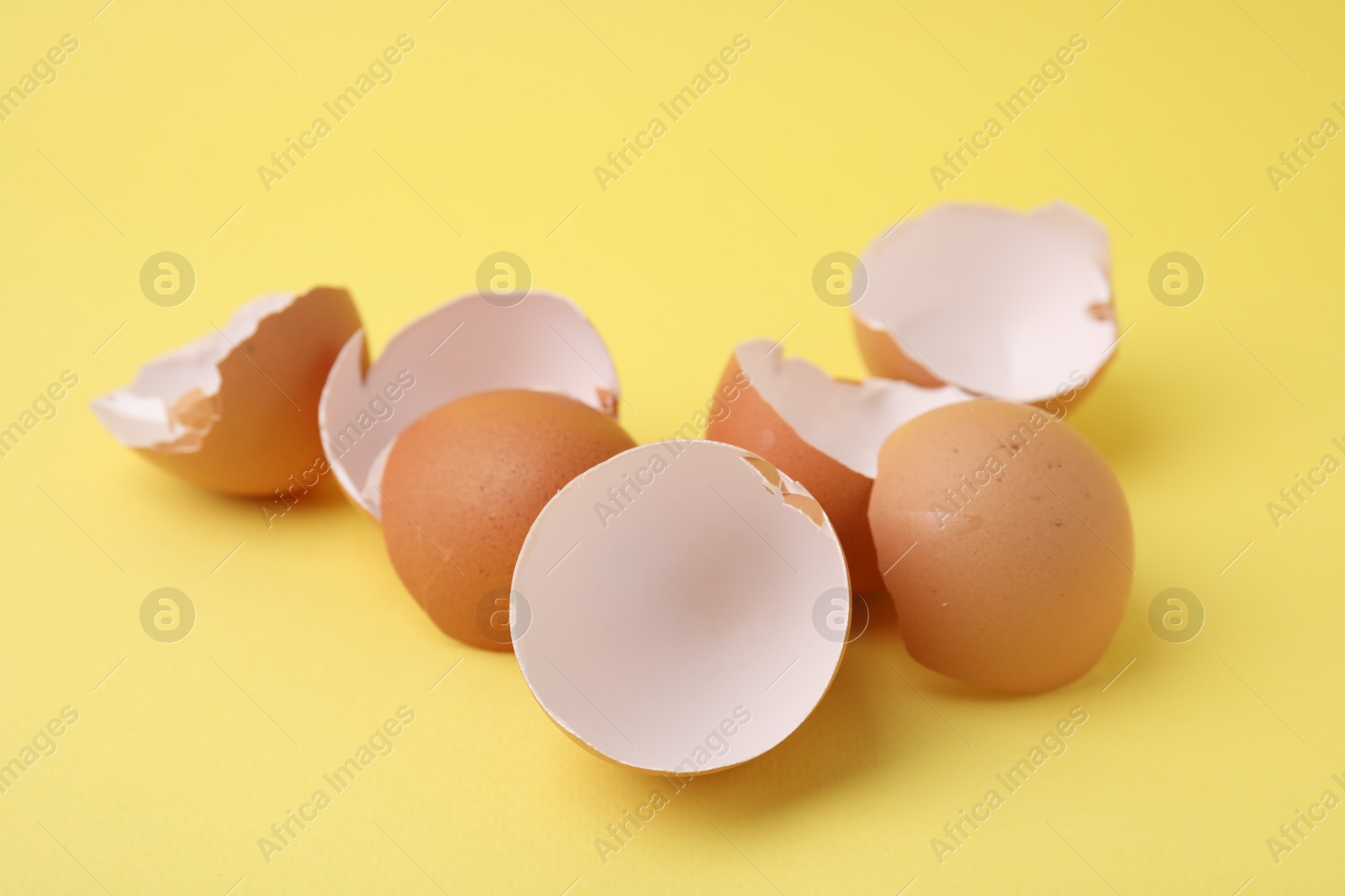 Photo of Pile of broken eggshells on yellow background, closeup