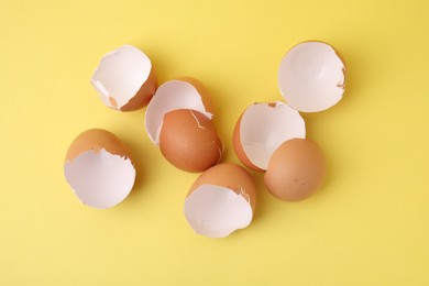 Photo of Pile of broken eggshells on yellow background, top view