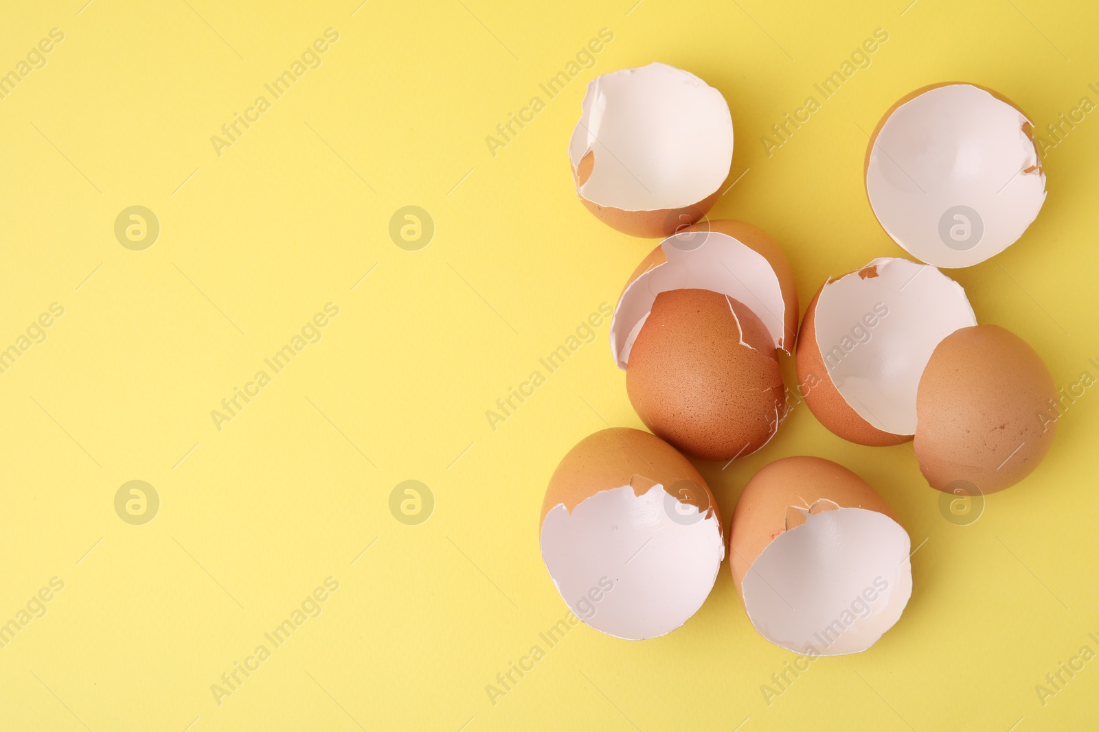 Photo of Pile of broken eggshells on yellow background, top view. Space for text