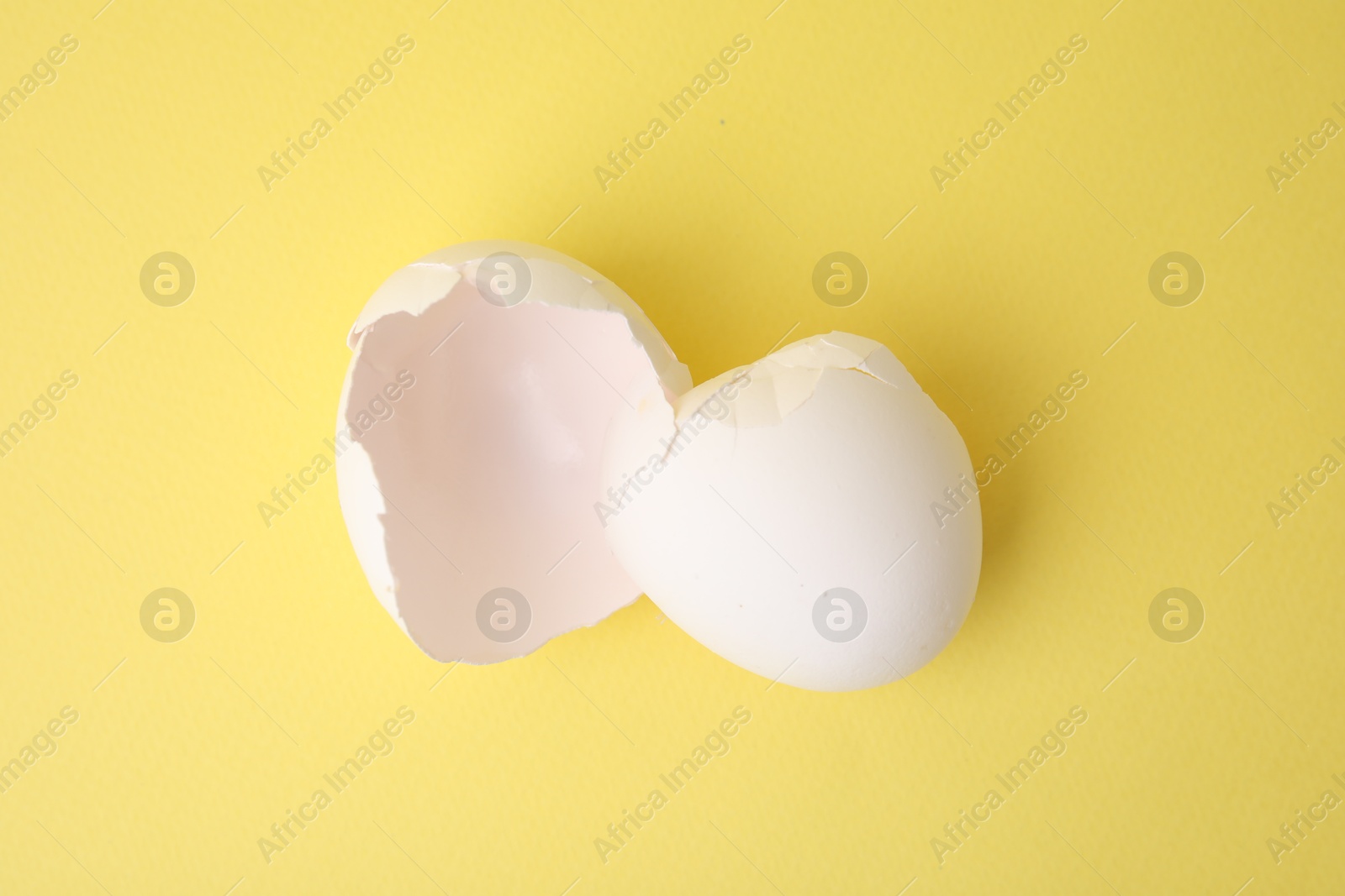 Photo of Pieces of broken eggshells on yellow background, top view