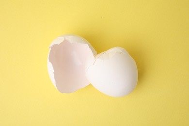 Photo of Pieces of broken eggshells on yellow background, top view