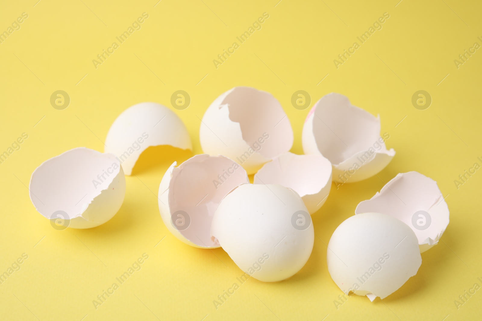 Photo of Pile of broken eggshells on yellow background, closeup