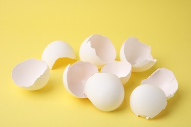 Photo of Pile of broken eggshells on yellow background, closeup