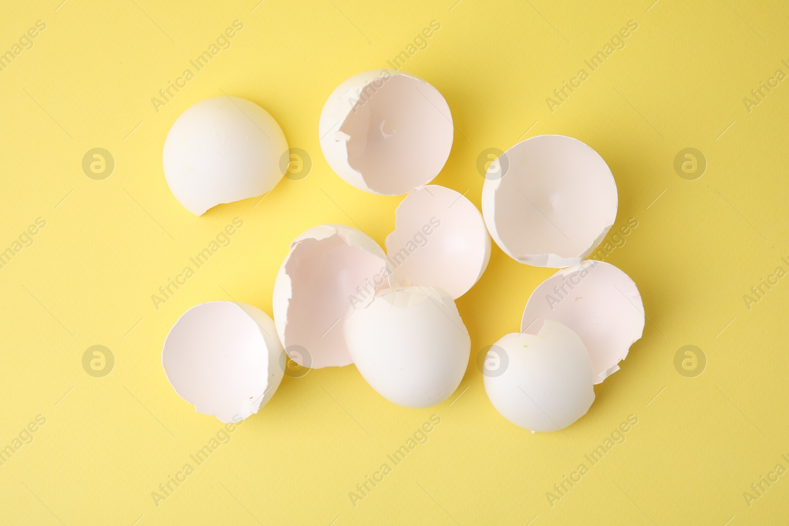 Photo of Pile of broken eggshells on yellow background, top view