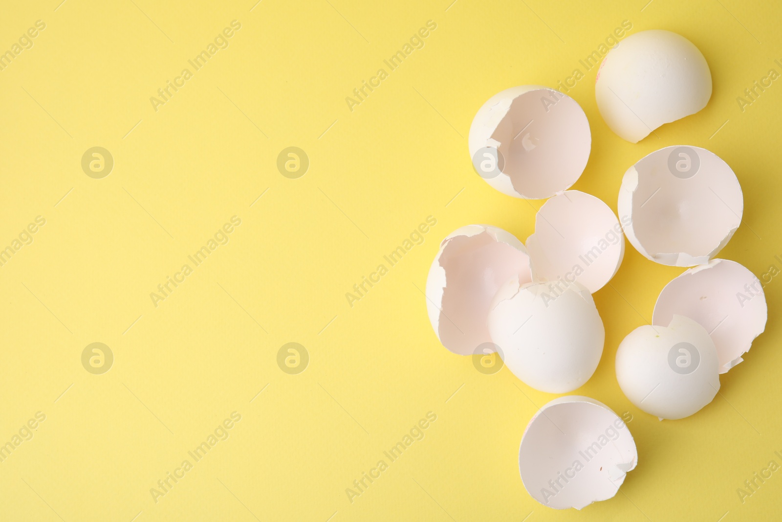 Photo of Pile of broken eggshells on yellow background, top view. Space for text