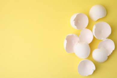 Photo of Pile of broken eggshells on yellow background, top view. Space for text