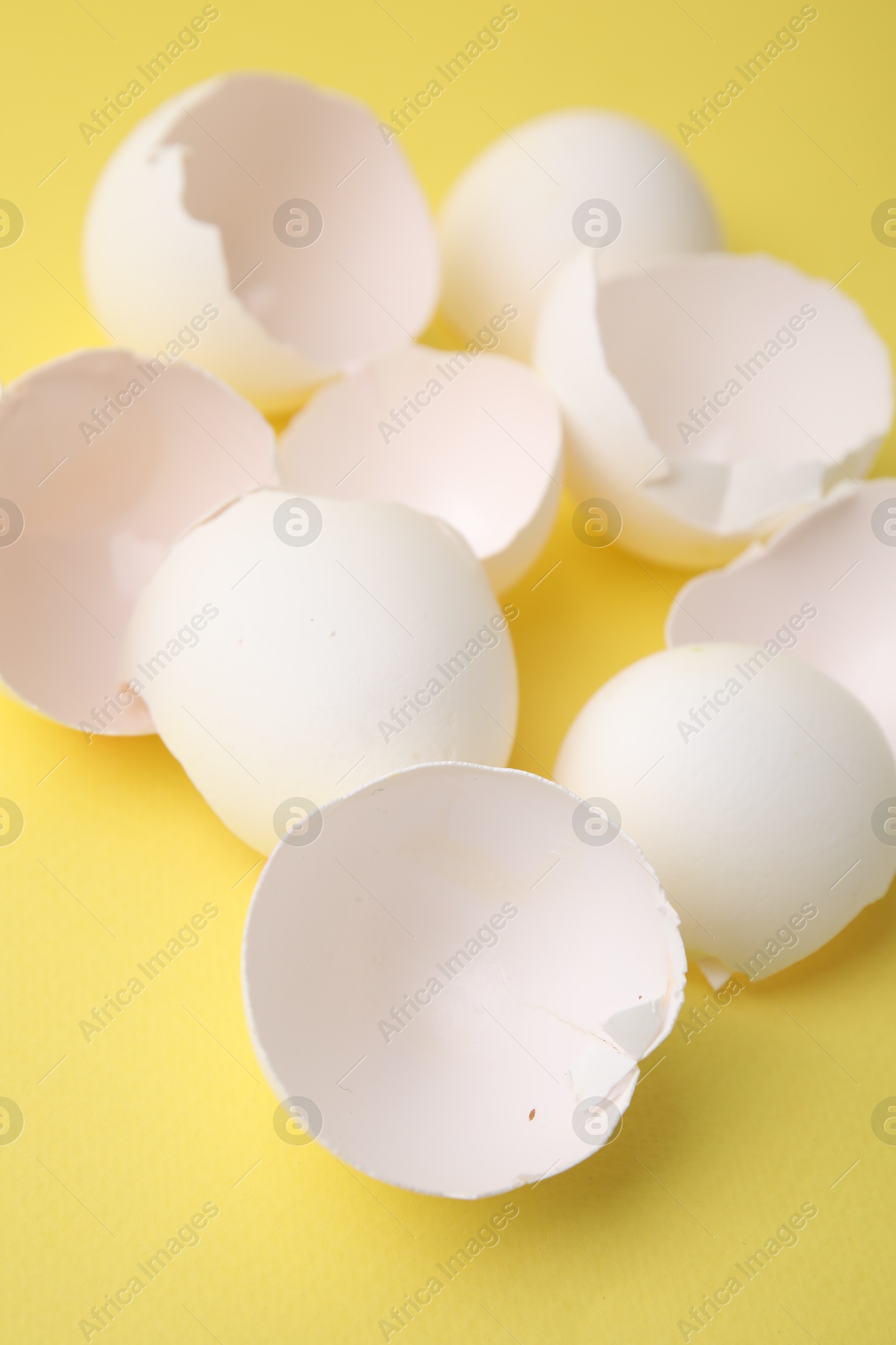 Photo of Pile of broken eggshells on yellow background, closeup