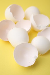 Photo of Pile of broken eggshells on yellow background, closeup