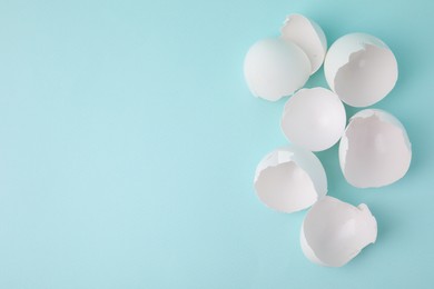 Photo of Broken eggshells on light blue background, top view. Space for text