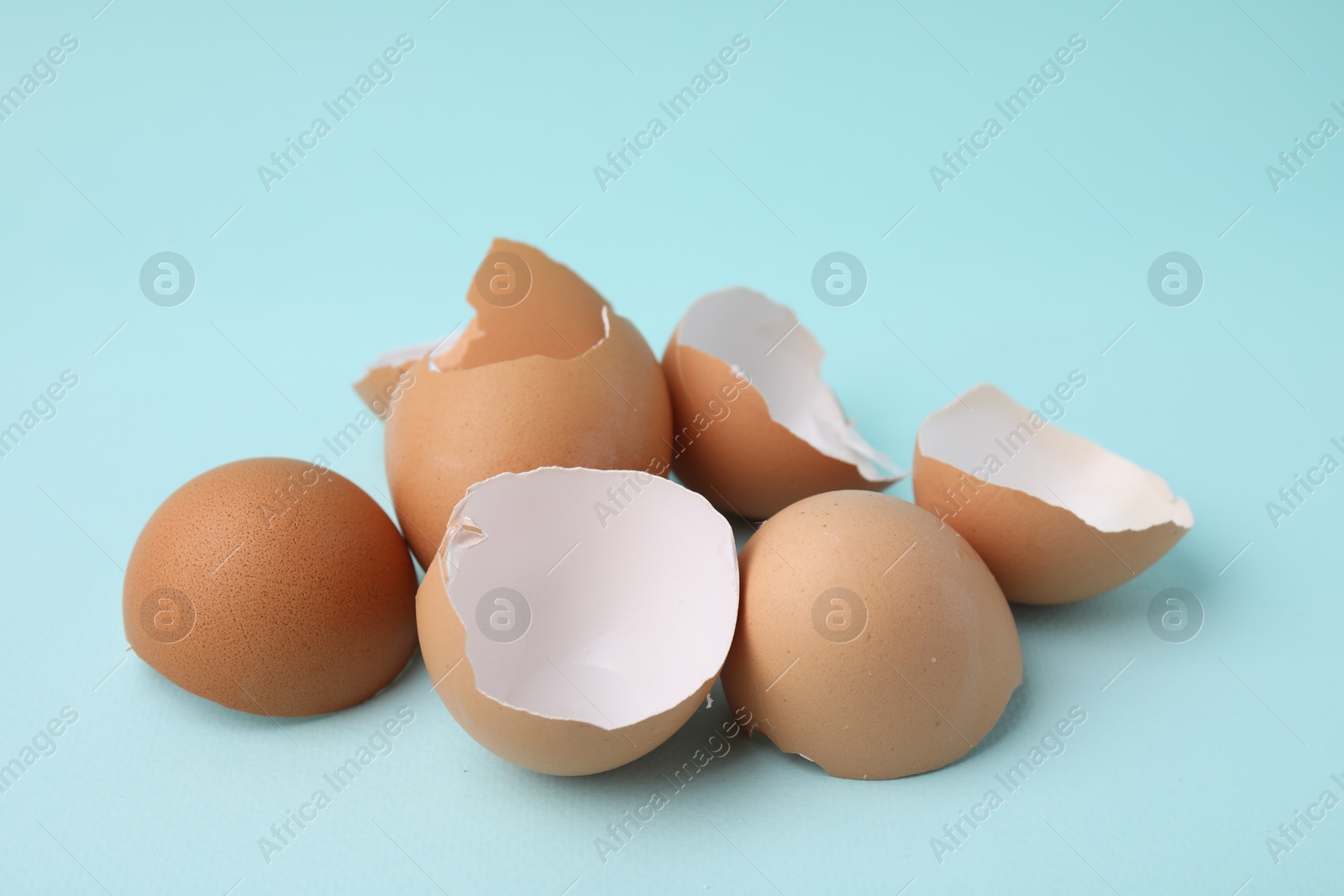 Photo of Pile of broken eggshells on light blue background, closeup