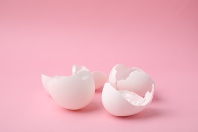 Photo of Pieces of broken eggshells on pink background, closeup