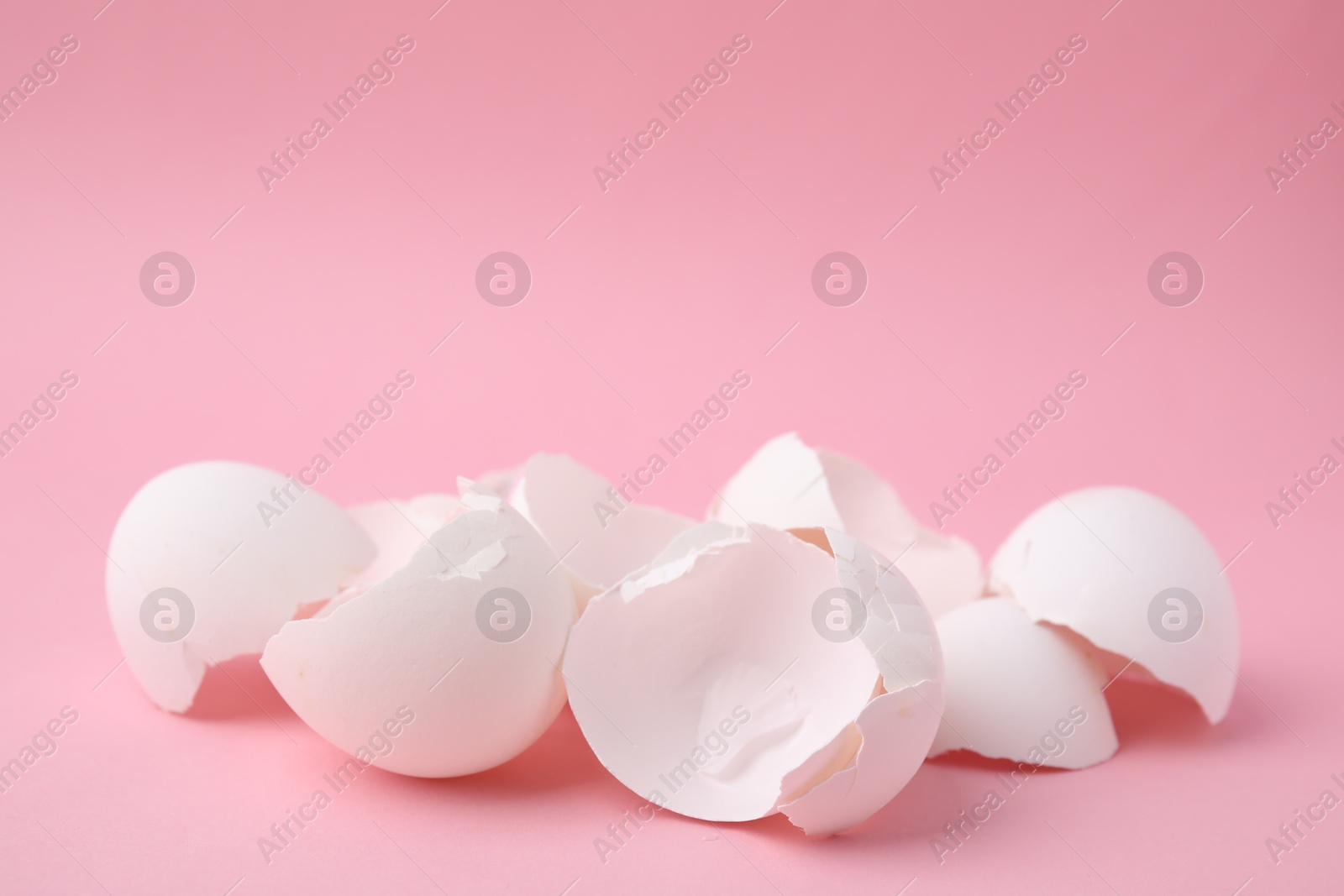 Photo of Pile of broken eggshells on pink background, closeup