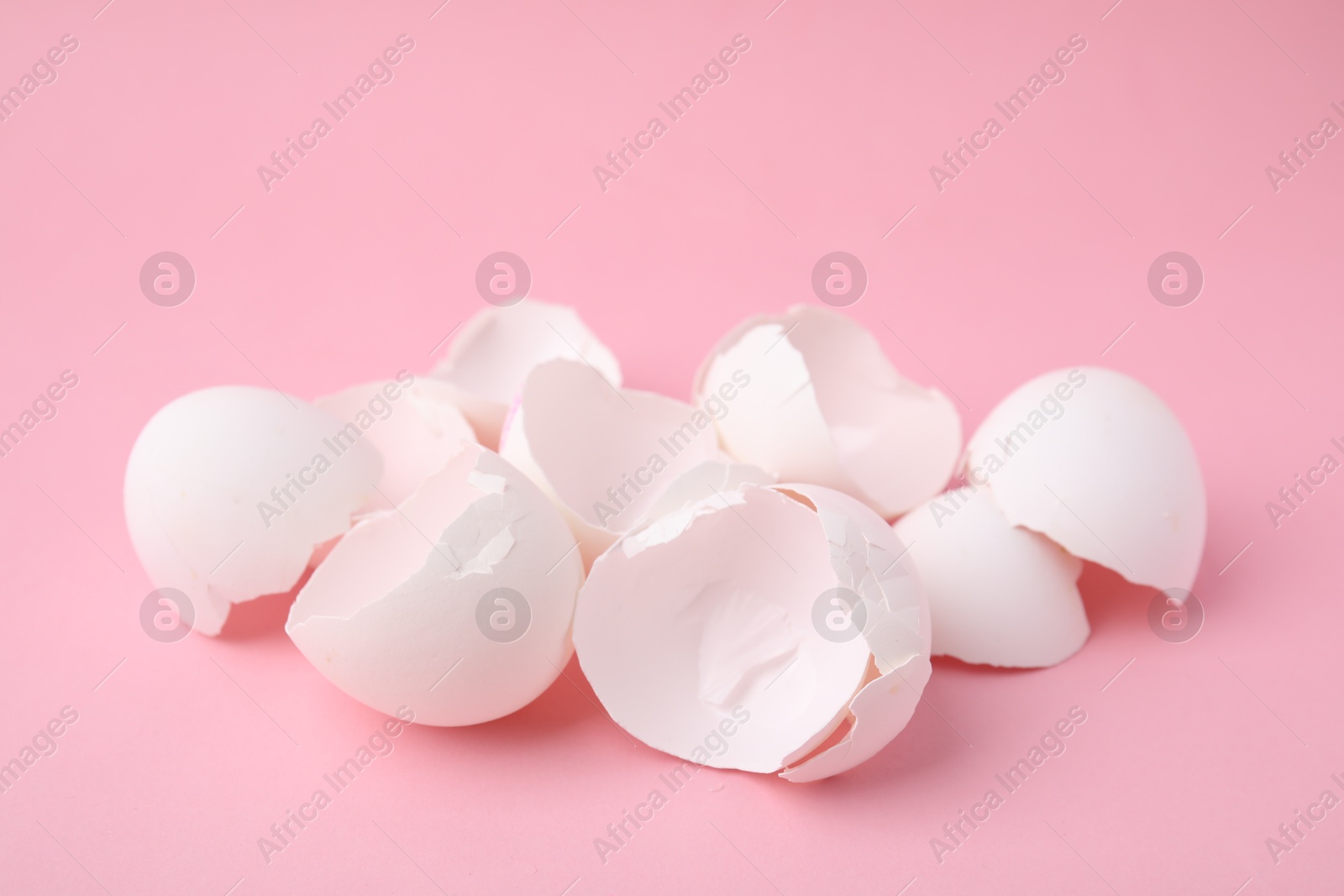 Photo of Pile of broken eggshells on pink background, closeup