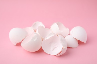 Photo of Pile of broken eggshells on pink background, closeup