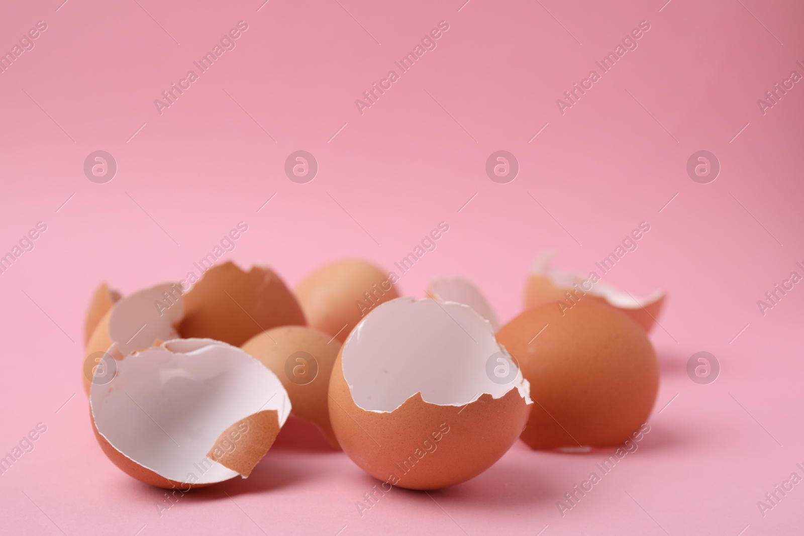 Photo of Pile of broken eggshells on pink background, closeup