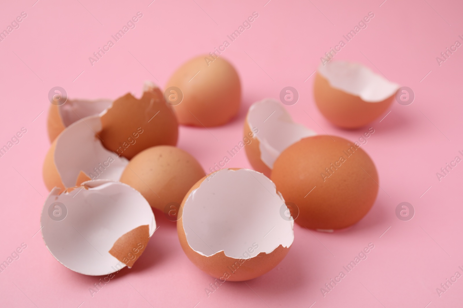 Photo of Pile of broken eggshells on pink background, closeup